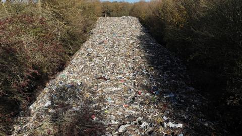 A huge pile of rubbish stretching into the distance with trees on either side
