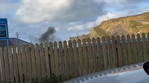 A plume of black smoke rises towards the sky after a controlled explosion took place in Portreath when an unexploded World War Two shell was found in a stream.