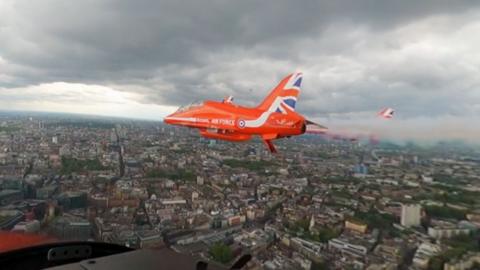 A Red Arrow flies above London on a gloomy grey skied day.