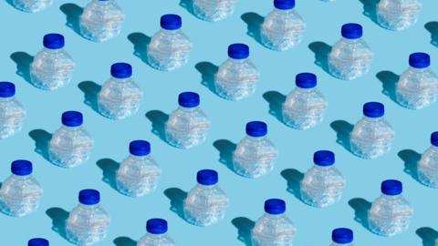rows of crushed single-use plastic water bottles all with dark blue lids. Sitting on a pale blue background. 