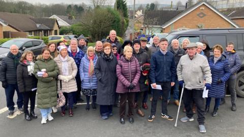 Around 30 people standing in the road in Valley Gardens, Hapton, facing the camera. Their homes are in the background.