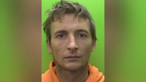 Custody image of Christopher Swift who has unkempt hair and is wearing a dirty orange hoodie