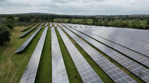 A solar farm with lines of panels in a green field