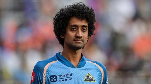 R Sai Kishore standing on the pitch wearing a jersey for Gujarat Titans during a match in 2025