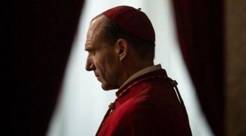 Ralph Fiennes' character wearing red papal regalia with his eyes closed in prayer