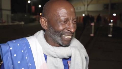 Ipswich Town fan smiles outside the Southampton ground at night. He is wearing a club shirt.