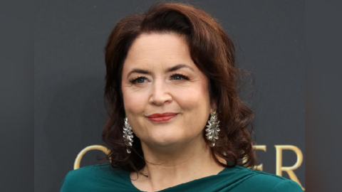 Ruth Jones in a green dress looking at the camera. She has silver dangly earrings in and her dark hair frames her face. 