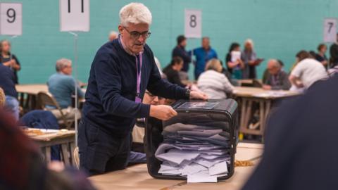 A man spilling a box of ballot papers onto a table