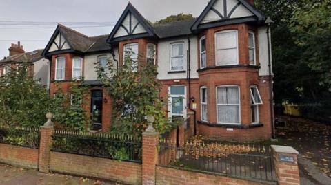 A former care home; it has red bricks, large front windows and a brick wall in the front.