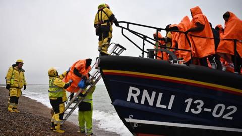 People from the RNLI help migrants off a rescue boat