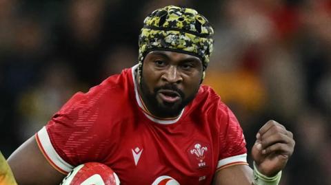Christ Tshiunza runs with the ball under his right arm for Wales against Australia in 2024