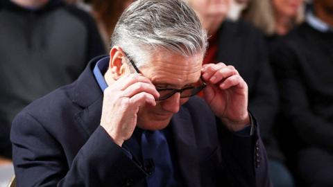 Close up of Keir Starmer adjusting his glasses looking down at the ground