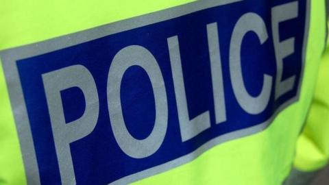The back of a police officer's fluorescent jacket showing the word "police" in silver letters on a dark blue background.