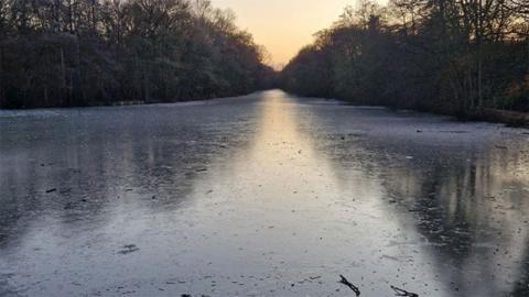 Lincolnshire Police picture of the frozen lake at Hartsholme Country Park. It show a stretch of water with trees along both banks.