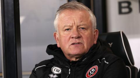 A concerned-looking Sheffield United manager Chris Wilder looks straight ahead from dug-out, wearing Club waterproof and badge