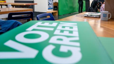 A blurry green sign which says Vote Greens