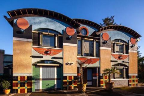 Exterior of a postmodern Egyptian-style property, featuring a winged solar disc over the main entrance, tartan pattern tiling along the base, and black columns topped with terracotta circles, representing the hieroglyph for the rising sun