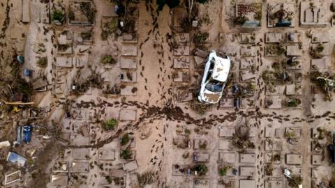 An aerial view taken with a drone shows a damaged car at a cemetery