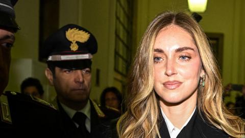 Chiara Ferragni walks into a courthouse in Milan with policemen behind her.