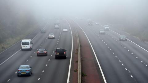 Vehicles travel in both directions of a motorway during foggy conditions