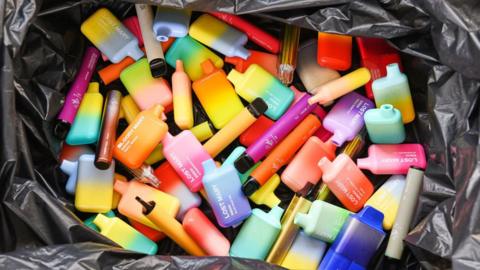 Brightly coloured single-use vapes in a recycling bin.