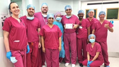 A team of 10 surgeons wearing pink scrubs standing inside a room. All are looking at the camera. 