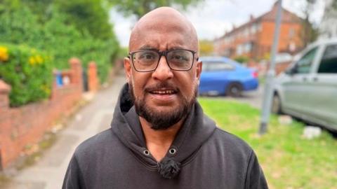 Man in a black hoodie and black-rimmed glasses. He is bald and has a short black beard.