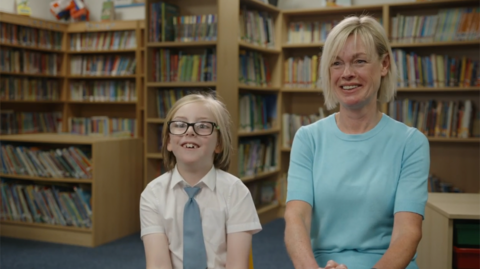 Student and teacher sit in front of a book case.