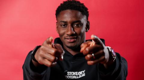 Djibril Soumare points at the camera with both hands and is wearing a black Stoke City hoodie