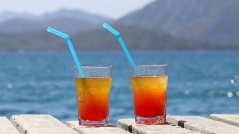 Two glasses with cocktail on a wooden pier on sea and mountains background