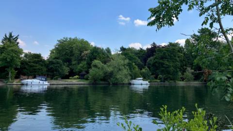 Two boats can be seen in the river at Old Windsor under blue skies and surrounded by trees and greenery