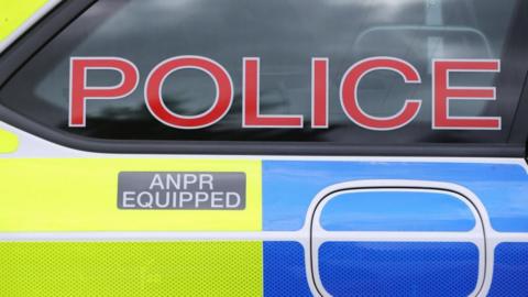 A close up of a police car. It is yellow and blue with red letters saying police. 