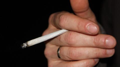 A young person's hand holding a roll up cigarette.