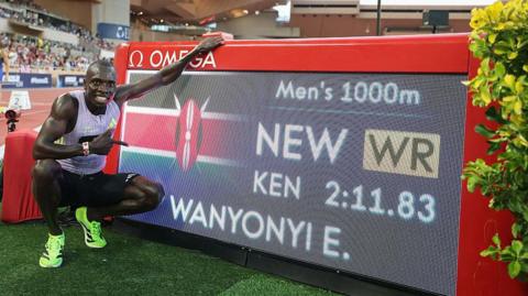 Emmanuel Wanyonyi poses for a photograph next to a digital screen showing his name and world record time after winning the 1,000m in Monaco