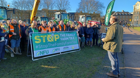 group of banner-holding protesters listening to a man in a green jacket