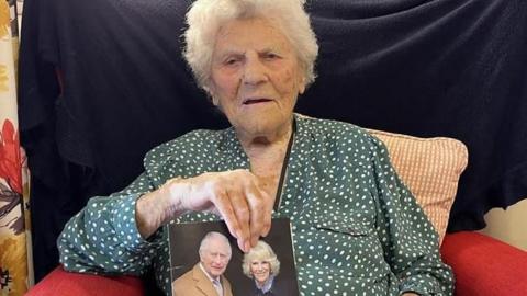 Ethel Caterham sat holding a card with a picture of the King and Queen on the cover.