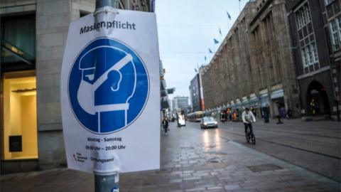 A sign indicating that face masks are mandatory hangs from a pole in the city centre of Bremen, Germany