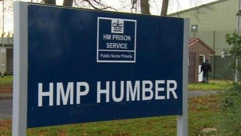 Sign outside Humber Prison. It is dark blue with white lettering with the HM Prison Service crown logo and the words HMP Humber.