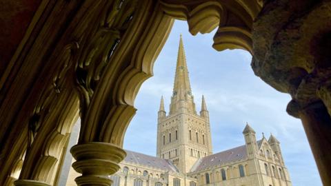 A church spire and blue sky can be seen through a stone archway