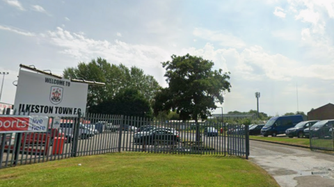 Sign which reads Ilkeston Town Football Club in front of a car park