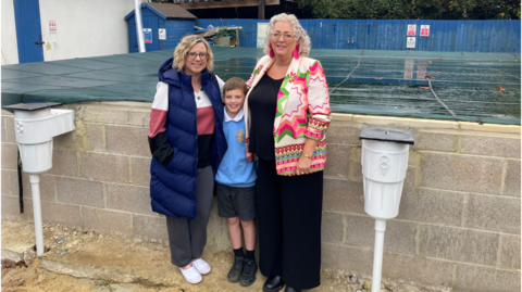 Leonard Stanley Primary School's Office manager Lisa Williams stands in front of the pool with head of the Parent Teacher Association Ali Higgins and her son who is a pupil at the school. The pool is still under construction and has a covering on it.