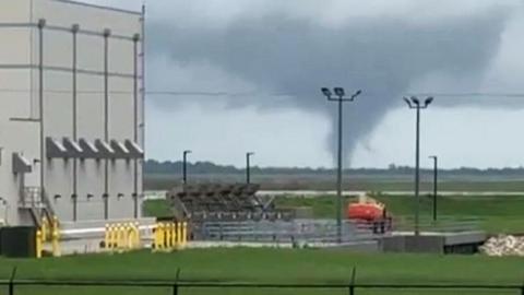 A tornado is seen in the background of a view of agricultural machinery and farmland, a grab from a video taken in Florida on Wednesday