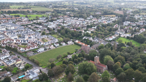 An aerial view of rows of houses surrounded by fields and trees.