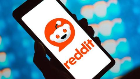 A hand holding a phone with the Reddit logo on it