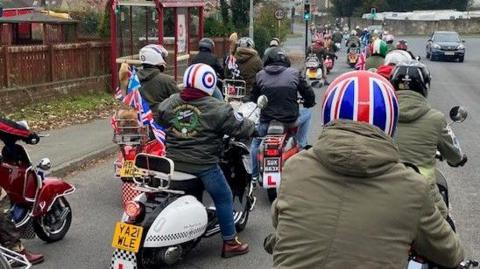 A group of scooters set off wearing parkas and helmets with Union Jacks and mod designs