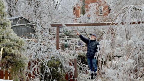 Man pointing at ice covered trees in backyard