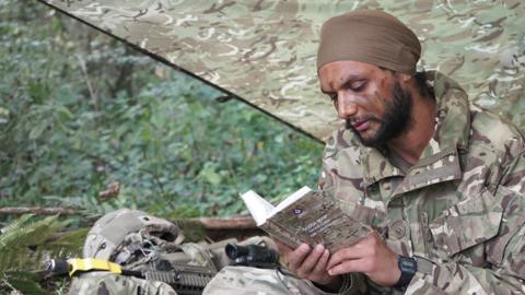 A soldier in uniform reads a Nitnem Gutka