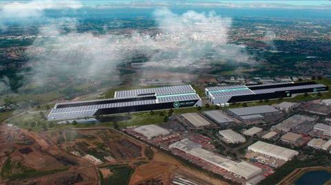 An aerial image with a CGI factory on a large space of land, next to several buildings