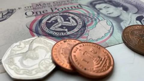 A close-up of a Manx £1 note, with two 1p coins and a 50p coin on top of it.