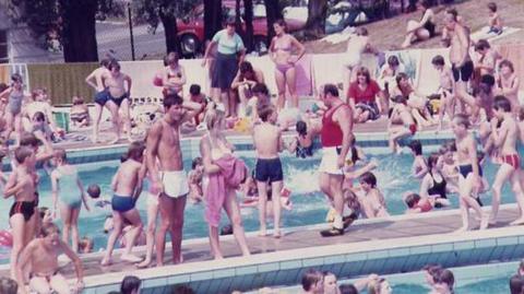 Dozens of people standing around the shallow pool at Ipswich's outdoor Broomhill Pool. The edge of the main pool is in the foreground.
